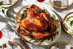 a roasted turkey on a platter surrounded by other plates and glasses with condiments