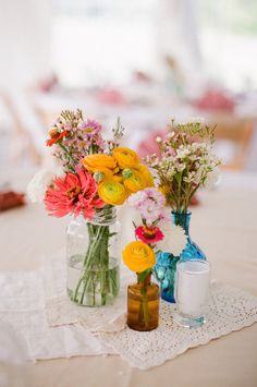 two vases filled with colorful flowers sitting on top of a white doily covered table