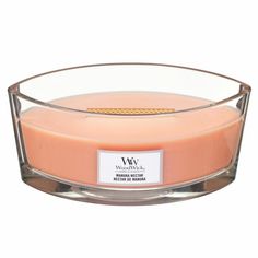 an orange candle in a clear glass bowl on a white background with a label that reads,