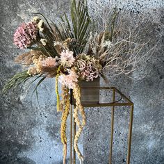 an arrangement of dried flowers in a vase on a metal stand against a concrete wall