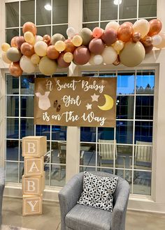 a baby is on the way sign in front of a window with balloons hanging above it