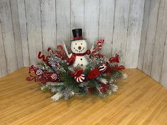 a snowman centerpiece with candy canes and greenery on a wooden table