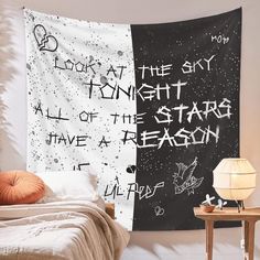 a bed with a black and white wall hanging next to a night sky tapestry on the wall