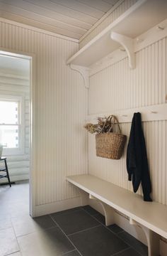 a white bench sitting under a window next to a basket on top of a shelf