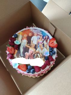 a birthday cake in a box with the image of friends and family on it is surrounded by berries, raspberries, and blueberries