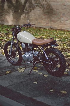 a white and brown motorcycle parked on the side of a road next to some leaves