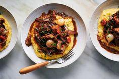 three white bowls filled with food on top of a marble counter next to utensils