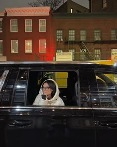 a woman sitting in the driver's seat of a black car on a city street