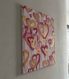 a painting hanging on the side of a wall with hearts painted all over it in pink, yellow and red