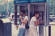 two people standing next to each other at a public phone booth