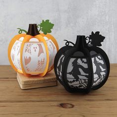 two paper pumpkins sitting next to each other on a wooden table with white and black designs