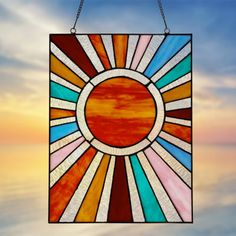 a stained glass sunburst hanging on a chain in front of a sunset sky