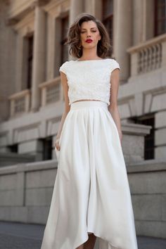 a woman wearing a white dress and heels standing in front of a building with her hand on her hip