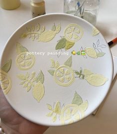 a person holding a white plate with lemons painted on it and the words pottery painting