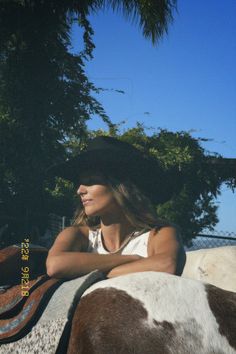 a woman wearing a cowboy hat sitting on top of a brown and white horse with trees in the background