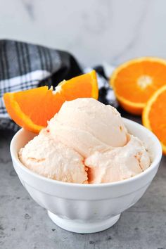 an orange ice cream in a white bowl with slices of oranges on the side