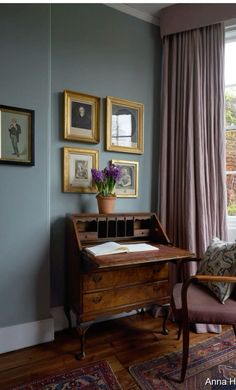 a chair and desk in front of a window with pictures on the wall behind it