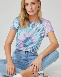 a young woman sitting on the ground with her legs crossed wearing white shoes and a tie - dyed t - shirt