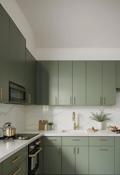 a kitchen with green cabinets and white counter tops, gold pulls on the cupboards