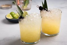 two glasses filled with drinks sitting on top of a table next to lime wedges