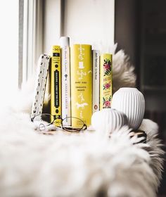 some books are lined up on a white furnishing next to a pair of eyeglasses