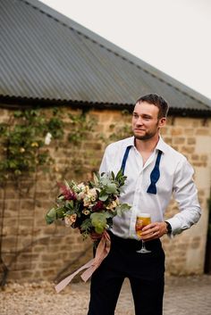 Groom in white shirt in undone bow tie holding the bridal bouquet with white and red flowers with pink ribbon and a glass of beer Lillian West Bridal, Groom And Groomsmen Outfits, Classic Romantic Style, Lillian West Wedding Dress, White And Red Flowers, Romantic Diy, Wedding Dress Photography, Groomsmen Outfits