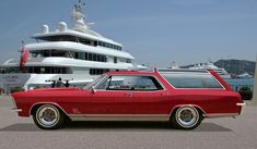 a red station wagon parked in front of a yacht