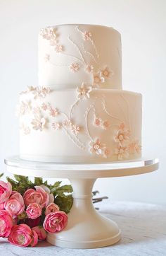 a three layer white wedding cake with pink flowers