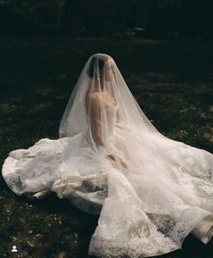 a woman in a wedding dress sitting on the ground with her veil over her head