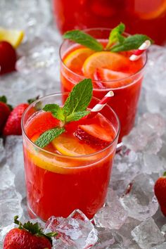 two glasses filled with red liquid and garnished with strawberries, lemons and mint