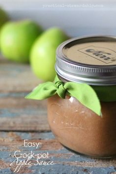 a jar filled with apple jam sitting on top of a wooden table next to green apples