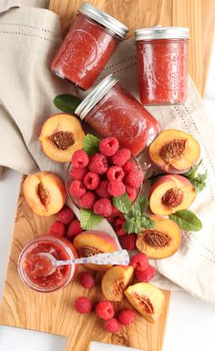 some raspberries and peaches are sitting on a cutting board next to jam