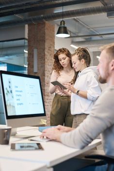 two women and a man looking at a computer screen in an office setting, while another woman looks on