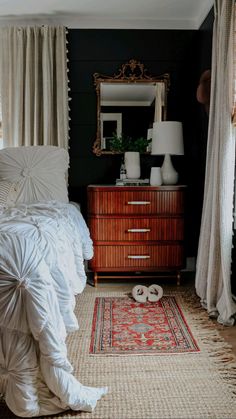 a white bed sitting next to a dresser in a bedroom under a window with curtains