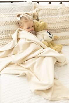 a baby wrapped in a blanket is laying on a bed next to a teddy bear