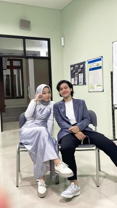 two women sitting on chairs in an office setting, one wearing a hijab