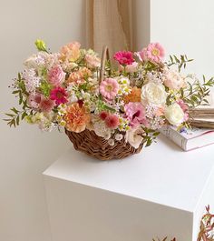 a basket filled with lots of flowers sitting on top of a white table next to a window