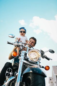 a man holding a baby on the back of a motorcycle with another person sitting on it