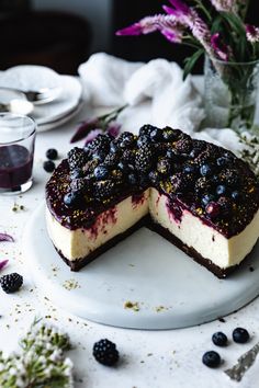 a cheesecake with blueberries and blackberries is on a plate next to flowers