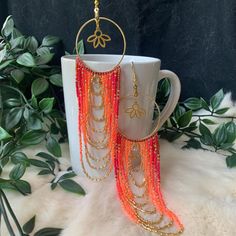 a pair of orange and gold beaded earrings hanging from a cup