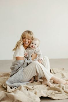 a woman holding a baby wrapped in a blanket on top of a bed next to a white wall