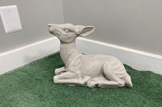 a statue of a fawn sitting on the ground next to a light switch box