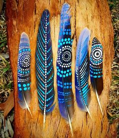 three blue feathers sitting on top of a piece of wood next to another feather that has been painted