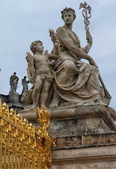 the statue is surrounded by many statues on top of each other in front of a golden fence