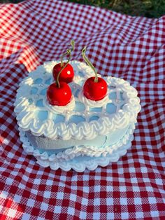 two cherries on top of a white cake sitting on a red and white checkered tablecloth