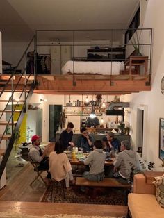 a group of people sitting around a table in a living room next to a staircase