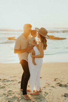 a man and woman standing on the beach with their baby in her arms, kissing