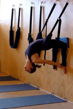 a man hanging upside down from a wall in a room with yoga mats on the floor