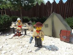 two legos are sitting in the sand near a tent and fire hydrant,