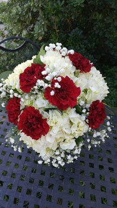 a bouquet of red and white flowers sitting on top of a metal table in front of some bushes